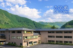 緑に囲まれた介護施設の建物外観。複数棟が立ち並ぶ全景写真。