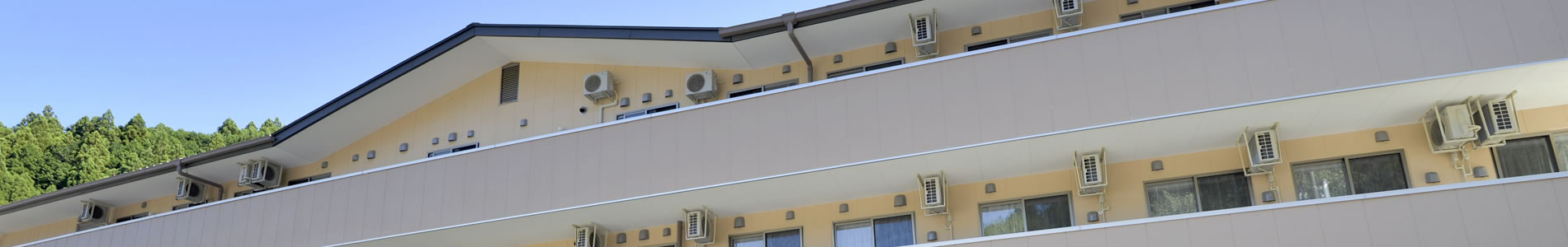 介護施設の建物外観。複数の小窓と空調室外機が見える2階部分の側面。